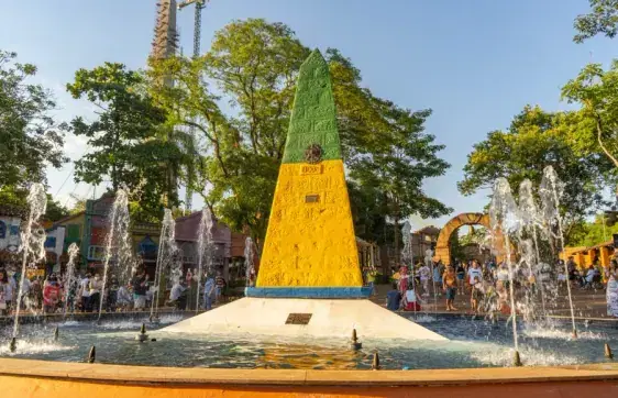 Obelisco verde e amarelo do Marco das Três Fronteiras, com fontes e pessoas ao redor